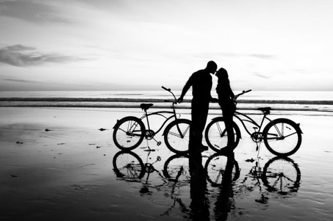 一对骑车的年轻情侣停下来在河边接吻的剪影照片